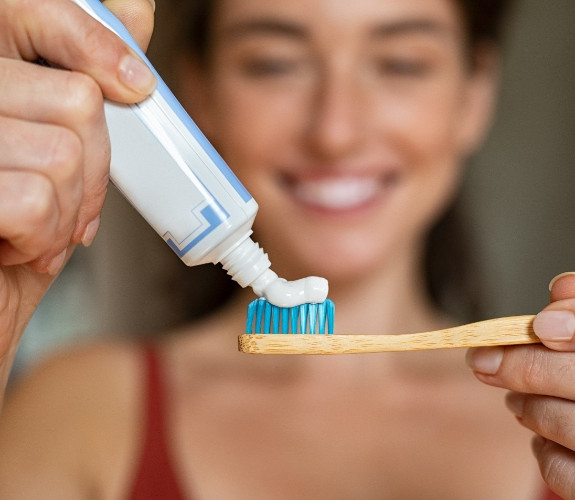 Woman placing toothpaste on her toothbrush in the bathroom